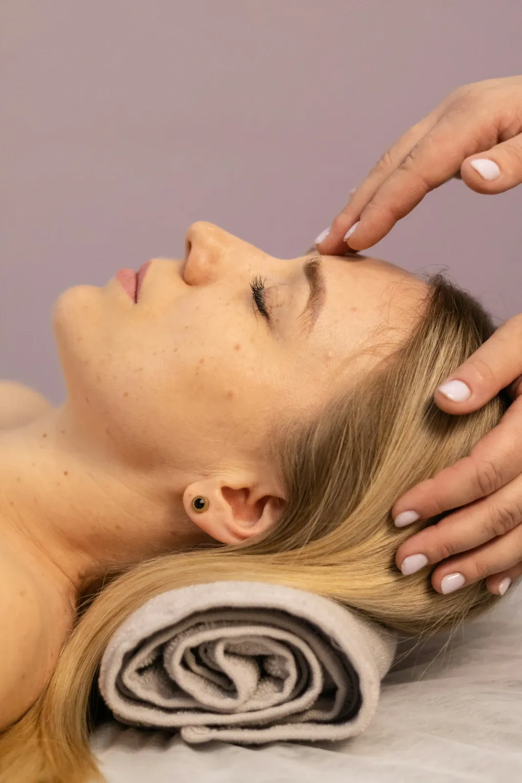 Mulher deitada de olhos fechados recebendo massagem facial suave nas têmporas