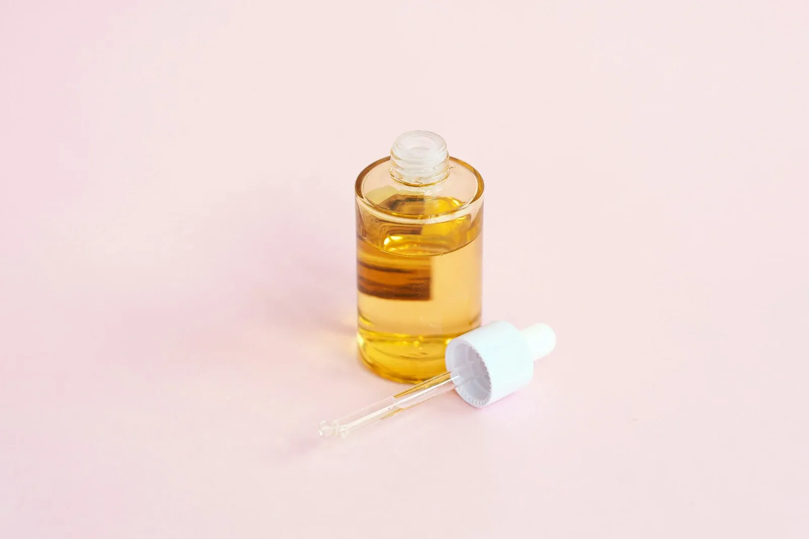 Frasco de vidro com sérum dourado e conta-gotas sobre uma superfície rosa-clara